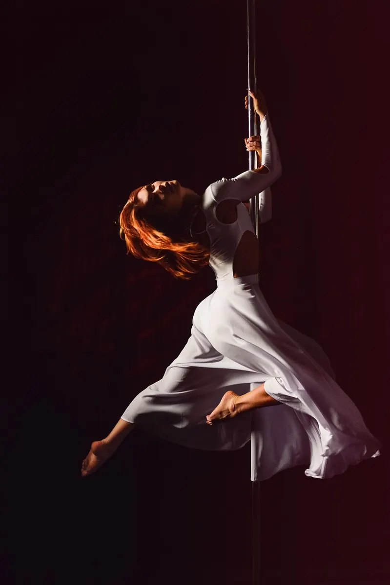 Danseuse de pole dance en robe blanche, figure artistique à la barre